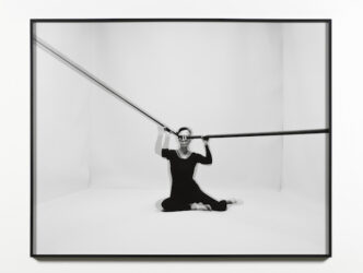 Purposefully blurred photograph of figure sitting in a room holding two long poles at their eyes