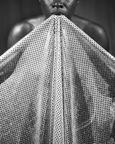 Black-and-white photograph of a figure with a sheet of fabric spilling out from their mouth