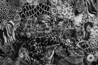 Black-and-white photograph of a tied bundle of clothing set against patterned fabric