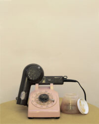 Color photographic still life of a pink phone with a black hair dryer in place of the receiver, with a jar of hair product to the right