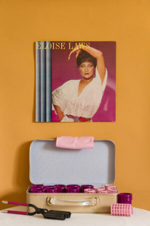 Color photograph of an album cover hanging on an orange wall above a hot roller set