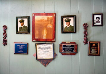 Color hotograph of a wall inside a home, covered with family photographs and plaques