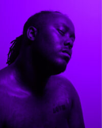 Color photograph of a person, their head tilted up and eyes closed, tinted purple