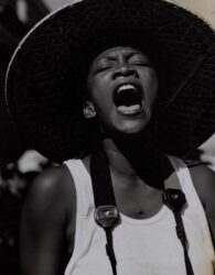 Black-and-white photograph of a woman in a wide-brimmed hat yelling in protest