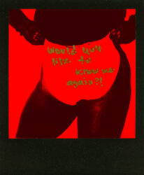 Black-and-red Polaroid of a person in white briefs, closer up on the underwear, with text in gold pen on the surface